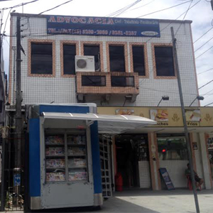 Em cima da padaria e da banca de revistas, várias janelas compõem a fachada do escritório em São Vicente/SP. 